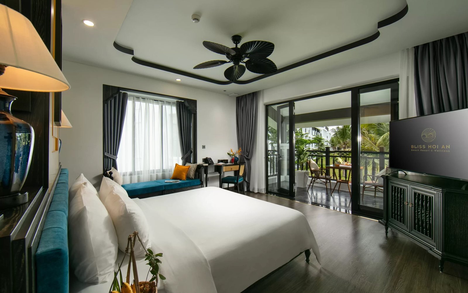 Hotel room in Hoi An with a writing desk by the window and a balcony table overlooking the garden